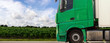 grüner Lastkraftwagen fährt an einem Maisfeld vorbei
