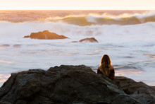 A Young Woman Watches In Awe Of A Violently Rough Ocean In Golden Light During Sunrise In Australia.