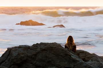 A young woman watches in awe of a violently rough ocean in golden light during sunrise in Australia.