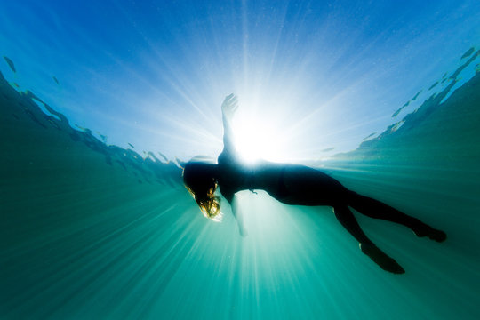 a beautiful woman floats on her back in the ocean as she is surrounded be bright ethereal light and 