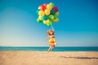 © Sunny studio - Happy child jumping with colorful balloons on sandy beach