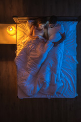 Wall Mural - The happy couple with a phone lay on a bed. Evening night time. View from above