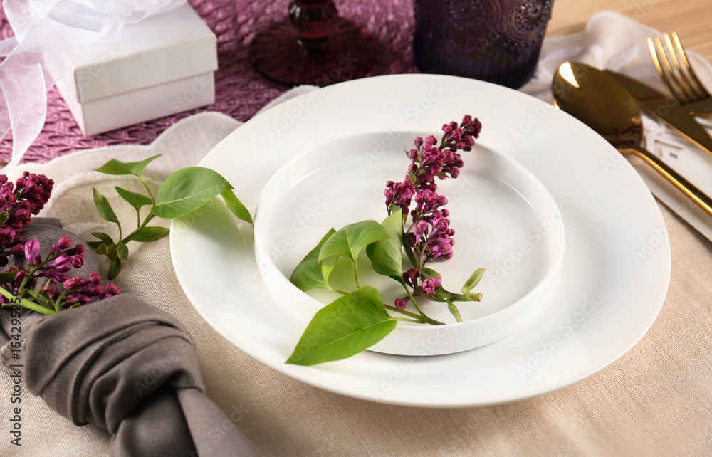 Table setting in lilac color and floral decor on white tablecloth