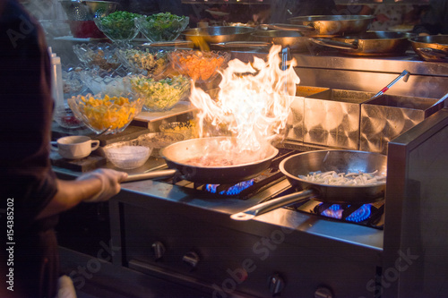 Zdjęcie XXL Szef kuchni w kuchni restauracji w piecu z patelni, robi flambe na jedzenie. niska selektywność skupienia ligth.