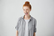 Childish and playful red haired teenage girl winking at camera, keeping mouth wide opened standing against blank studio wall background with copy space for your text or promotional information