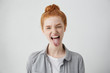 © WHstudio Leushin N - Naughty teenage girl with ginger hair and freckles misbehaving, sticking out her tongue at camera as a sign of disobedience, protest and disrespect. Human emotions, reactions, feelings and attitude