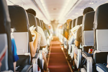 Passenger Seat, Interior Of Airplane With Passengers Sitting On Seats And Stewardess Walking The Aisle In Background. Travel Concept,vintage Color,selective Focus