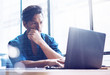 © SFIO CRACHO - Young elegant banking finance analyst working at sunny office on laptop while sitting at wooden table.Businessman analyze stock reports.Blurred background,horizontal.