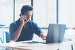 © SFIO CRACHO - Elegant businessman working at sunny work place on laptop while sitting at the wooden table.Man using smartphone and analyze document on computer notebook.Blurred background.Horizontal.