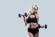 © liliyabatyrova - beautiful blonde girl slim figure, with makeup, in a black sports underwear is with dumbbells in hands, looking down, gray background, isolate, fitness, cross fit, sports,