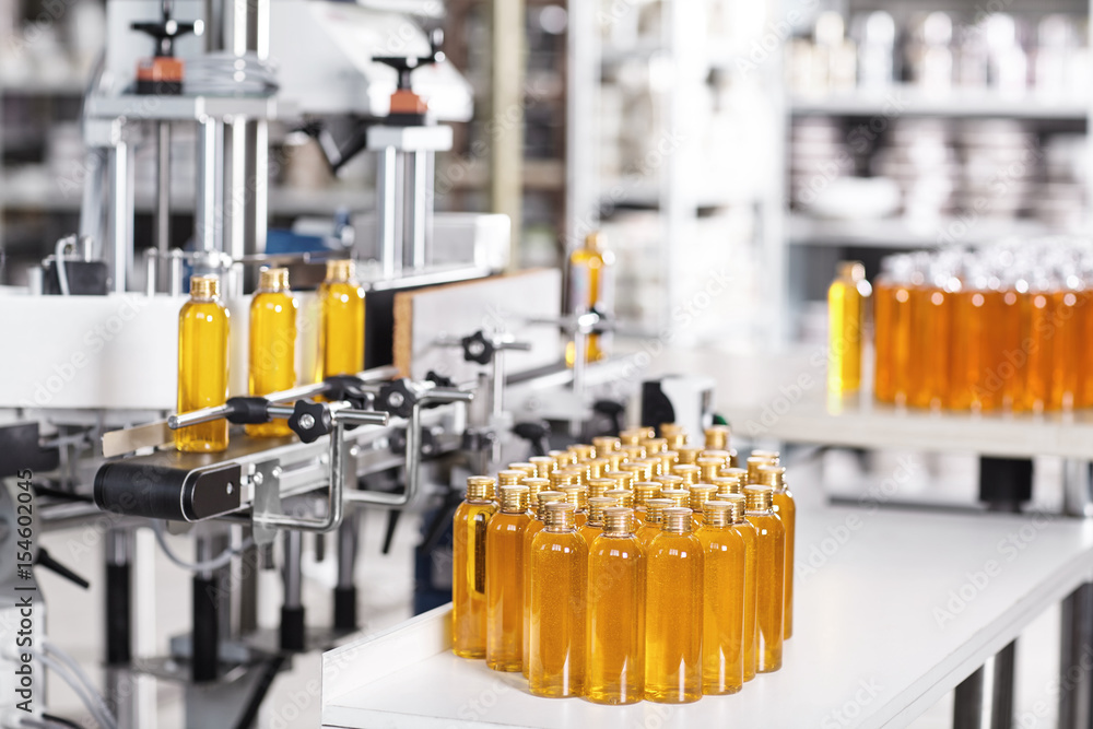 Batching Cosmetics Cosmetics factory. Bottling line filled with yellow shampoo. Automated ...