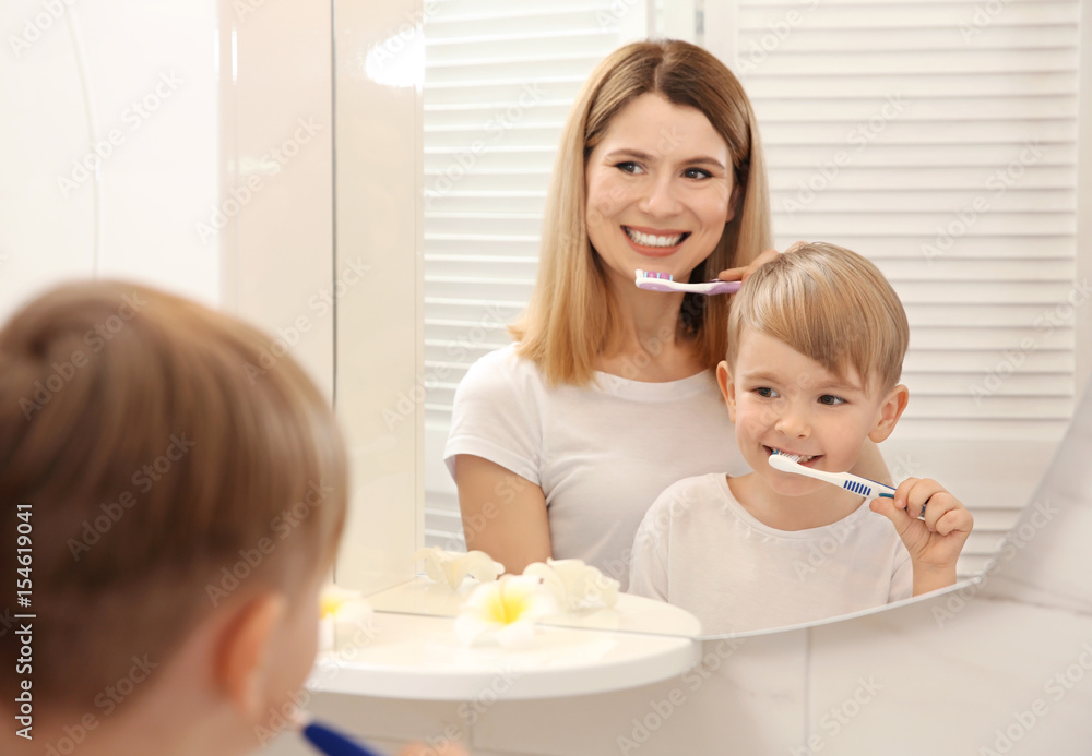 Beautiful mother with her son brushing teeth and looking in mirror