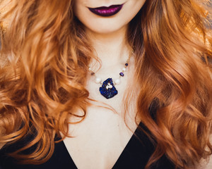 close-up portrait of young beautiful red-haired girl in the image of a Gothic witch on Halloween on a background of wax candles, fire, magic crystals and stones in the black dress conjures