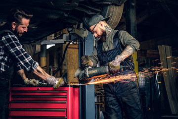 Two b mechanics working with an angle grinder in a garage.