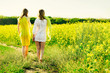 Mom with daughter or two sisters or girlfriends in dresses go against the background of a yellow field. Back-view