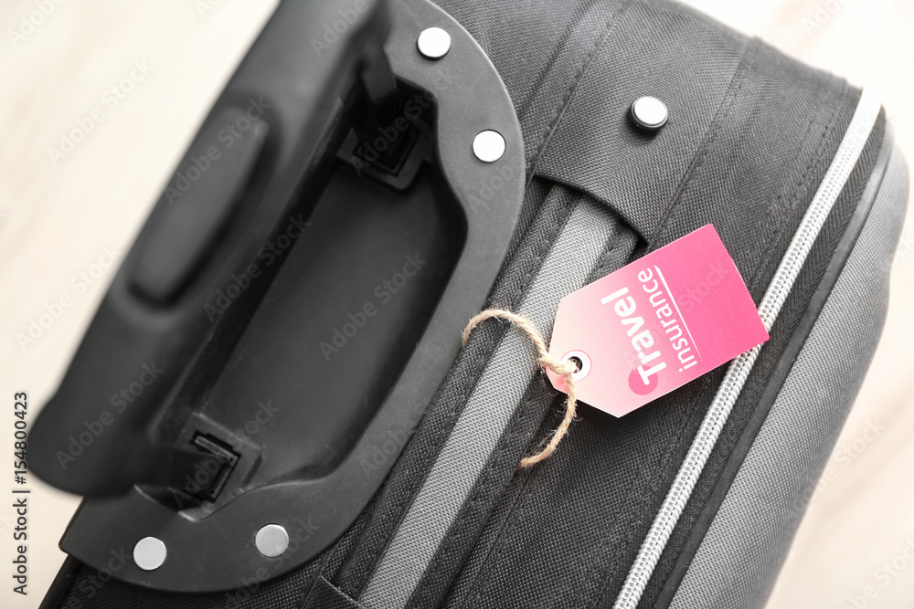 Black suitcase with label, closeup. TRAVEL INSURANCE concept