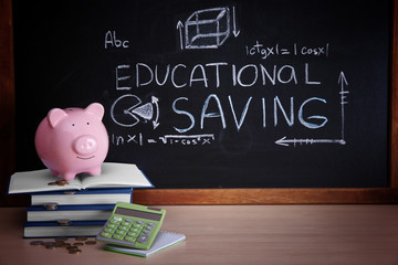 Wall Mural - Piggy bank with books, coins and calculator on blackboard background. Educational savings concept