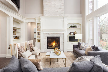 beautiful living room in new luxury home with fireplace and roaring fire. large bank of windows hint