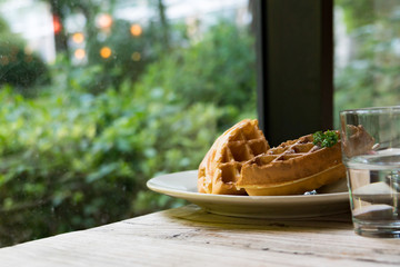 2 pieces of waffle with a glass of water on the wooden table - apply filter