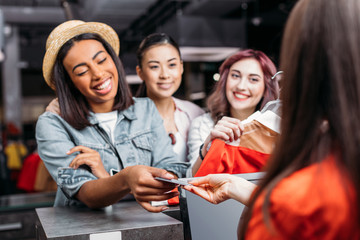 Happy stylish young women paying with credit card in shopping mall, young girls shopping concept