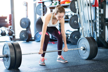 Wall Mural - Beautiful young fit woman in gym lifting heavy barbell