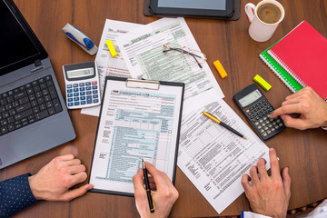 two people filling tax forms, helping each other.