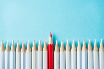 Business concept - lot of white pencils and color pencil on blue paper background. It's symbol of fight, leadership and communication.