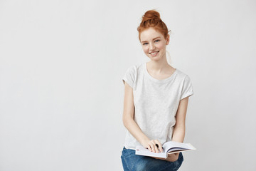 Sticker - Beautiful ginger student girl smiling holding book looking at camera.