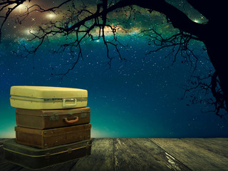 Stacked leather luggage on wood plank with stars in night sky background. Travel concept. Fantasy lanscape.