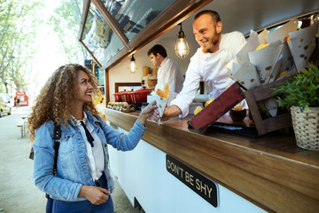 Beautiful young woman buying barbecue potatoes on a food truck.