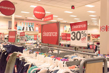 Red Clearance Sign For 30% Off On Cloth Rack With Variety Of Women Apparel In Retail Store In America.
