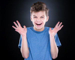 Wall Mural - Emotional portrait of irritated shouting teen boy. Furious teenager screaming and looking with anger away. Handsome outraged child shouting out loud, on black background.