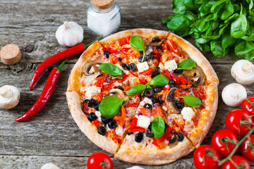 Homemade Pizza with tomato sauce, artichoke hearts, olives, Parmacotto, fresh mozzarella, parmesan and basil on the grey wooden background