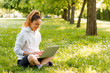 © bnenin - Young woman with laptop sitting on green grass in the park