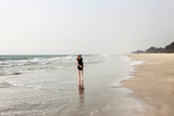 Fototapeta Konie - girl in black dress walking on a sand shore