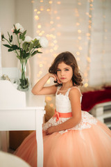 Wall Mural - Little beautiful girl with brown hair in a Peach-colored dress. Poses for a photographer