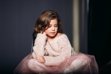 Wall Mural - Little beautiful girl with brown hair in a light sweater and with a skirt of tulle.Studio. A princess poses for a photographer.