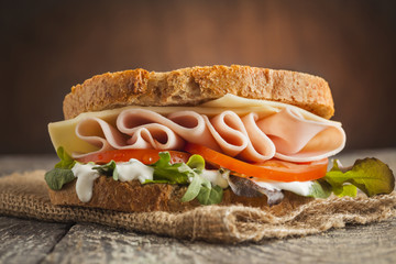 Tasty sandwich with ham, cheese, tomato and lettuce on wooden background