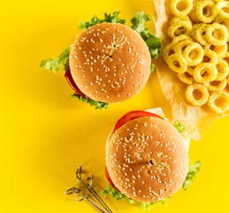 Sticker - Tasty fresh unhealthy hamburgers with ketchup and vegetables and chips on yellow vibrant bright background. Top View with Copy Space.