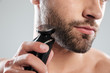 © Drobot Dean - Cropped image of a young bearded man using electric shaver