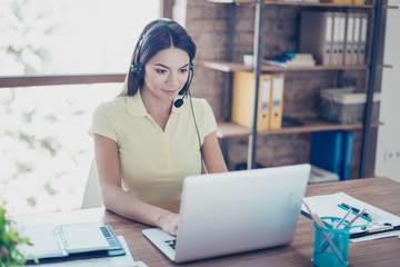 Successful young latin girl is talking to customer with headset on and putting data in her computer