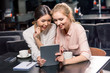 © LIGHTFIELD STUDIOS - Smiling young women using digital tablet while drinking coffee in cafe, lunch meeting concept