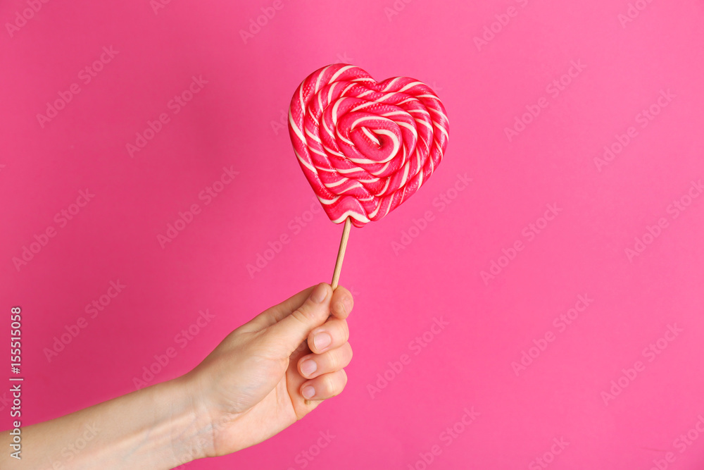 Female hand with tasty lollipop on color background