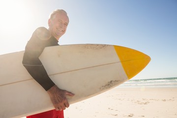 Canvas Print - Portrait of smiling senior man holding surfboard