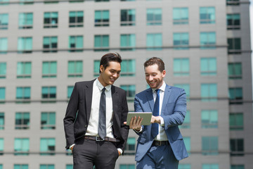 Wall Mural - Two Smiling Business Men Using Tablet and Walking