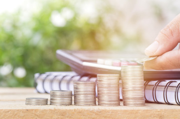 hand put money on stacked of coins  with book and calculator