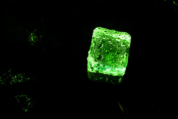 Green ice cubes on black wet table.