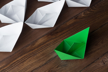 Business leadership concept with white and color paper boats on wooden table