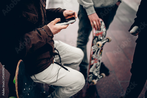 Zdjęcie XXL facet trzyma telefon na tle Przyjaciele firmy mężczyzn trzymając ręce deskorolki. Pojęcie grupa uliczna atleta uczni ogólnospołeczna sieć