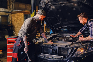 Two mechanics fixing car's engine in a garage.